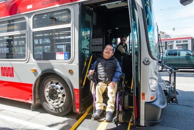 A customer in a wheelchair exits a bus while a driver deploys the lift