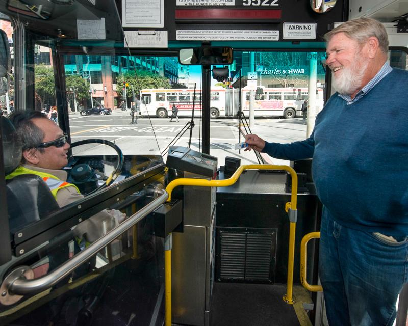 white haired man boarding Muni bus and showing driver a pass