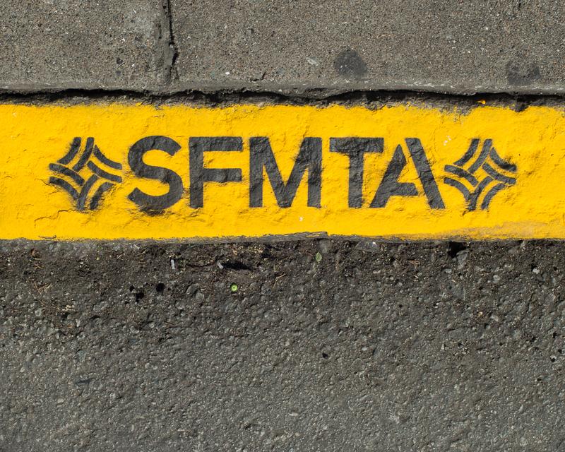 detail view of a yellow painted curb with letters SFMTA and SFMTA logo