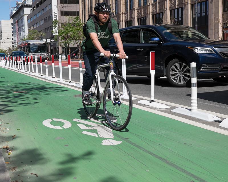 person riding bike in protected bike lane on market