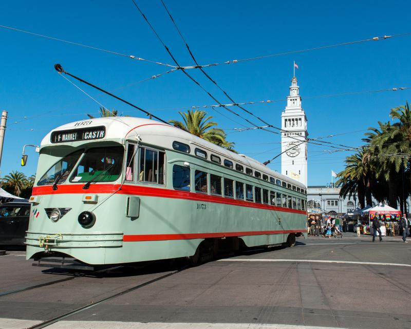 mint green streetcar with red striping and white roof in front of Ferry building on Market Street