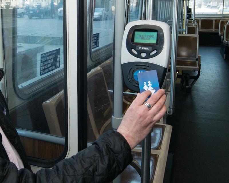Person sitting on a bus taps their clipper card.