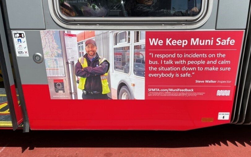 We see the side of a bus with a MuniSafe poster featuring a staff member. A quote on the poster reads: "I respond to incidents on the bus. I talk with people and calm the situation down to make sure everybody is safe."