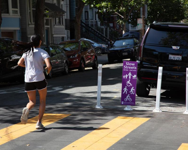 A person running on a Slow Street with a purple Slow Streets program sign
