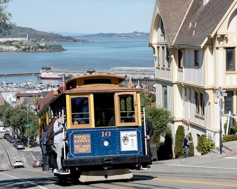 Color photo of cable car 16 climbing hill on Hyde Street with view of San Francisco Bay in background. 