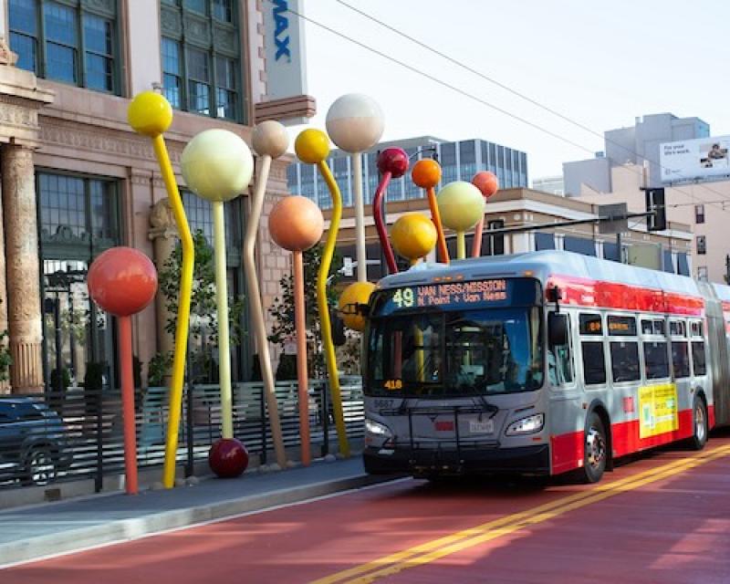 A bus driving down the new red bus rapid transit lane on Van Ness in front of a public art installation