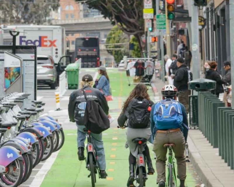 3 cyclists riding towards king street in the new 2-way protected bike lane. to the left is the lyft bike share docking station.