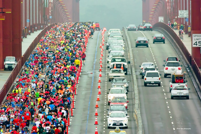 Thousands of runners in colorful atttire run across one side of the Golden Gate on an overcast morning.
