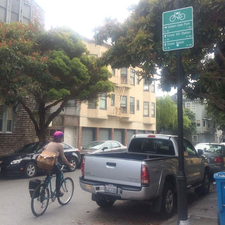 A woman bikes down a street past a bike wayfinding sign posted on a street light pole.