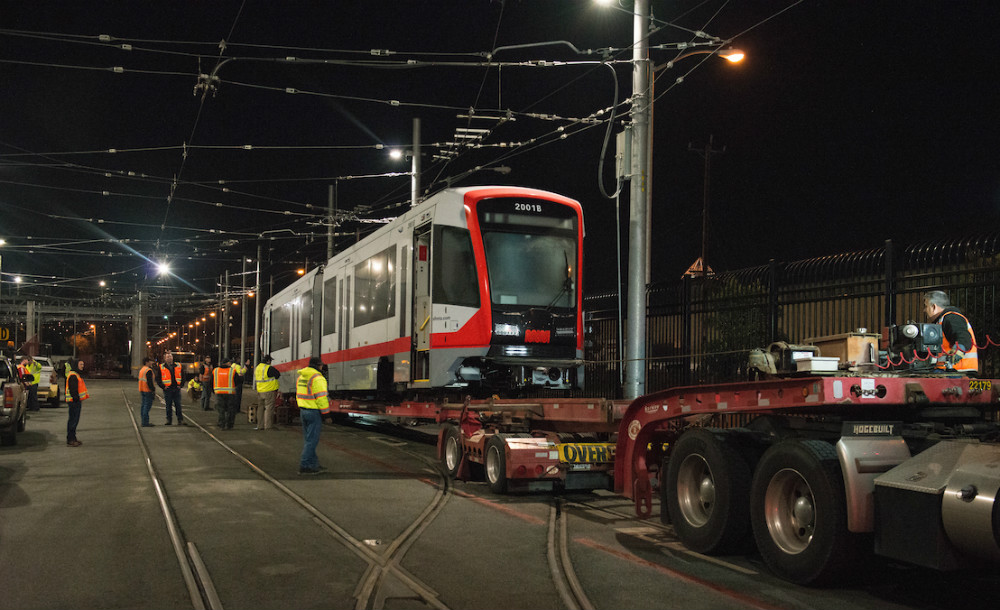 Crews offloading the new Muni train from a truck bed at night.