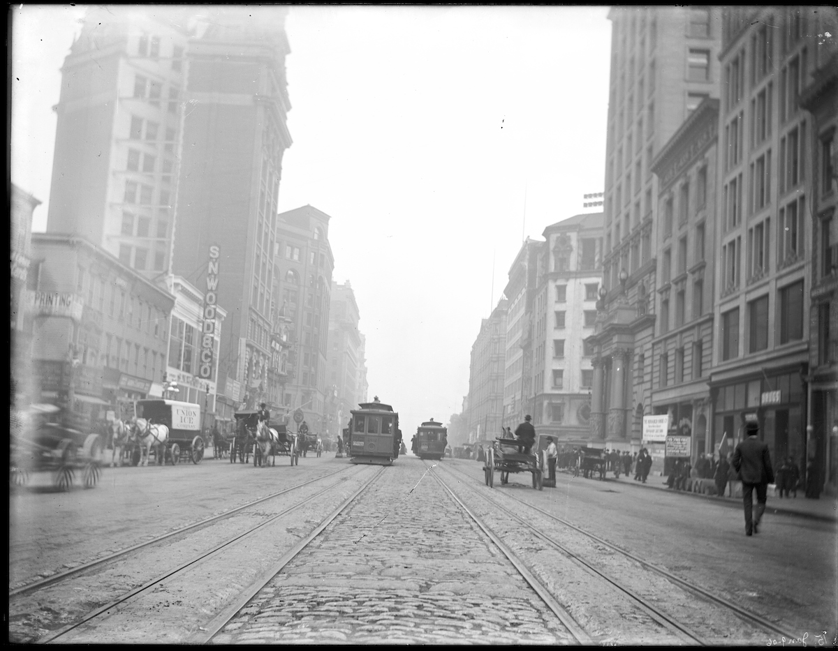 street scene with horse drawn carts, pedestrians, and cable cars