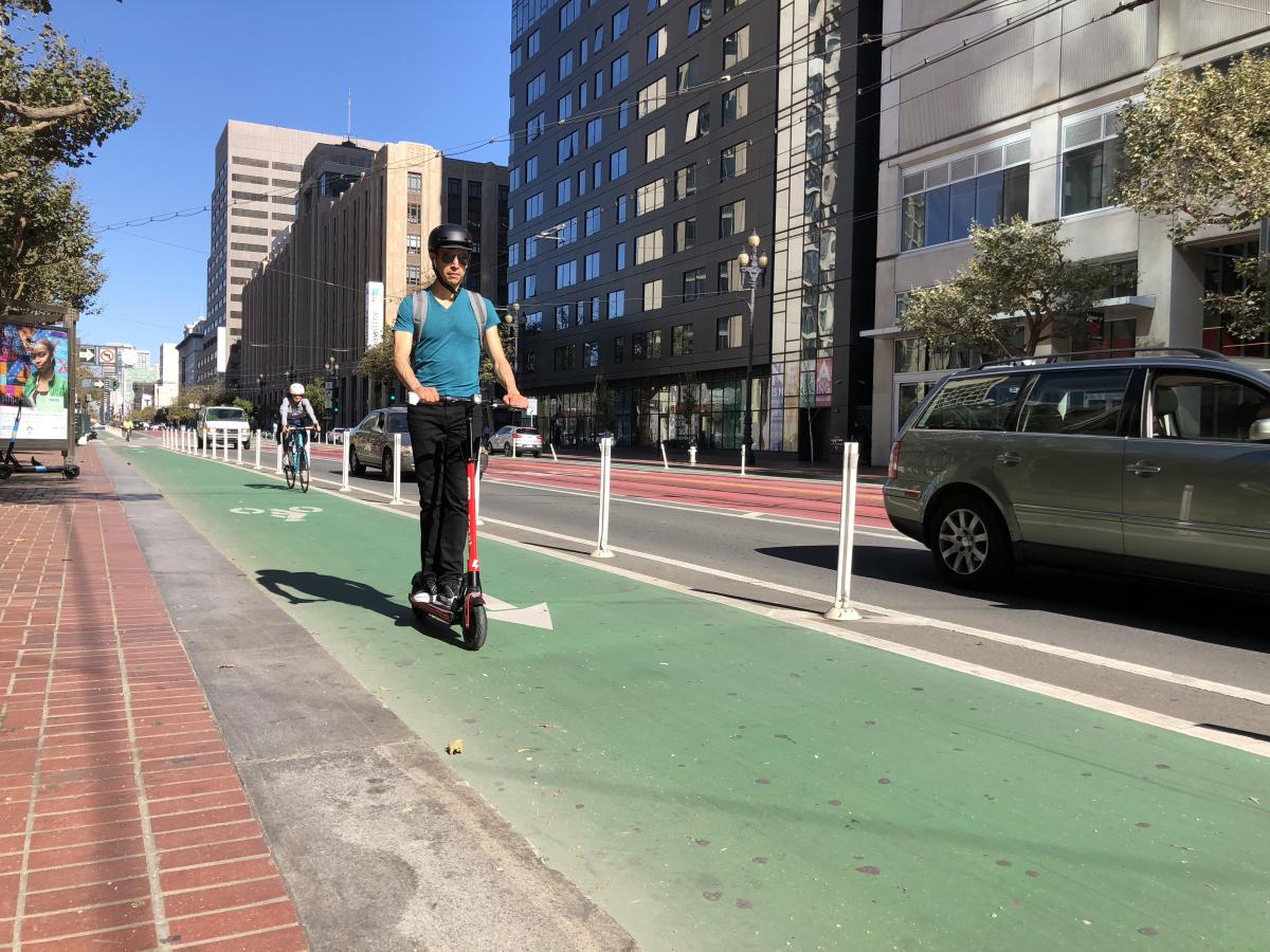 A person wearing a helmet rides a scooter in a bike lane