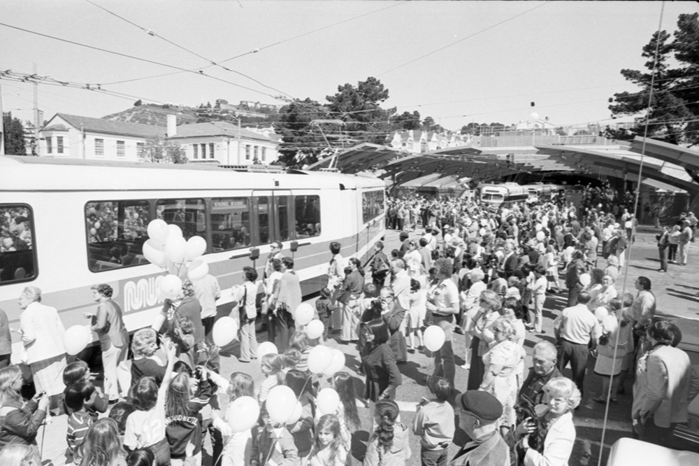 crowd of people with muni streetcars outside west portal station