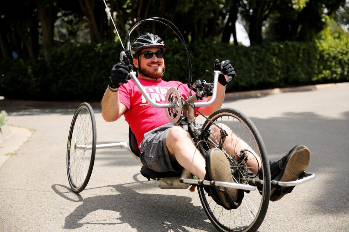 (Image: Kurt, smiling, sits in a recumbent foot-pedal bike, holding the bike’s handlebars.)