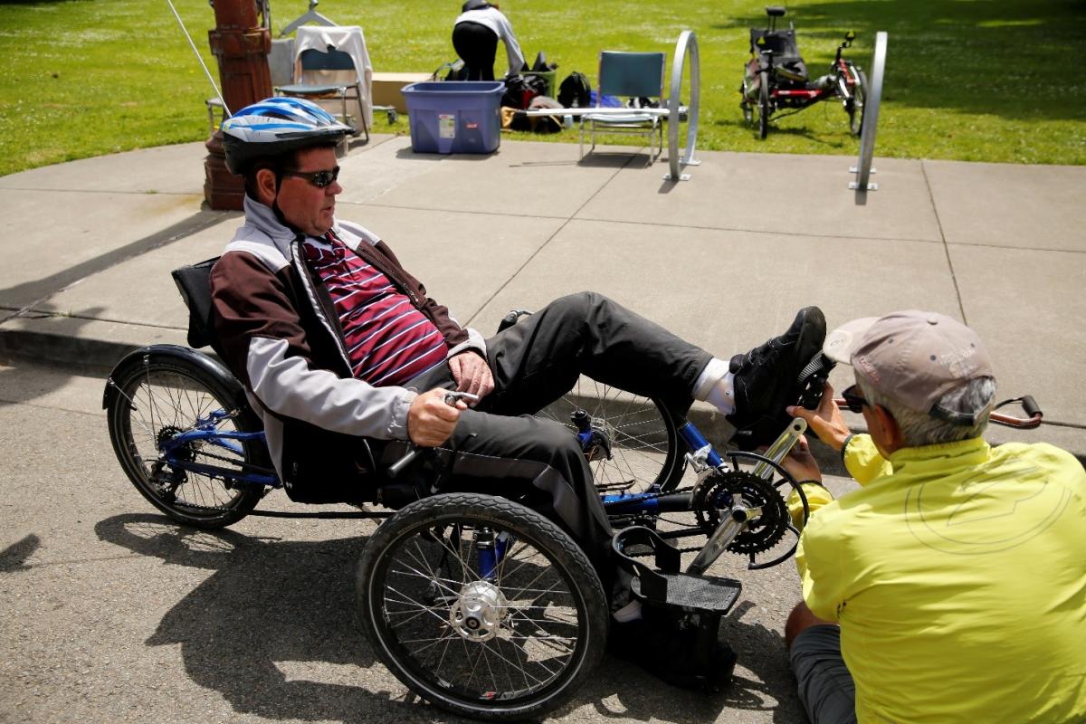 (Image: Finn, a BORP participant, is assisted by a BORP staff member while he is strapped into a recumbent trike.)
