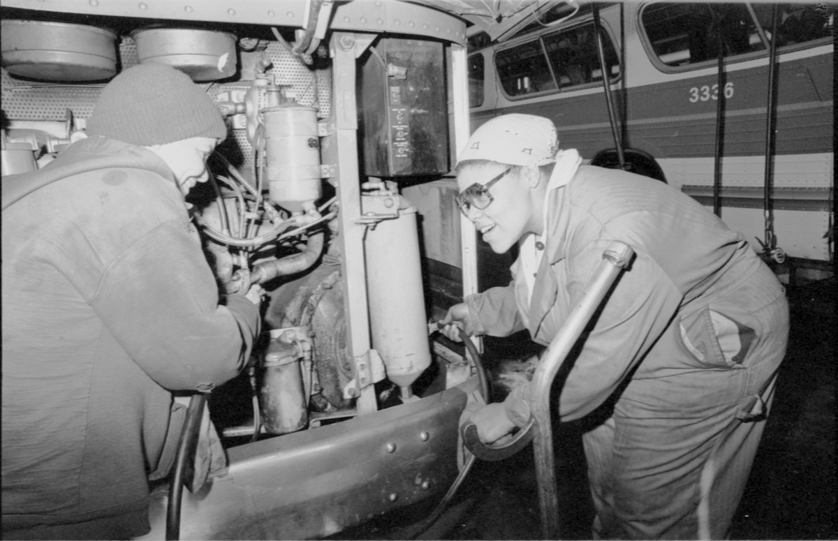two women standing at engine compartment of bus