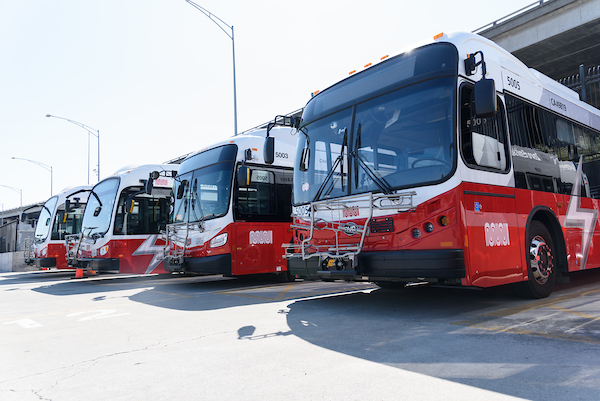 A bus yard with a close up shot of several parked Battery Electric Buses that are red and white.