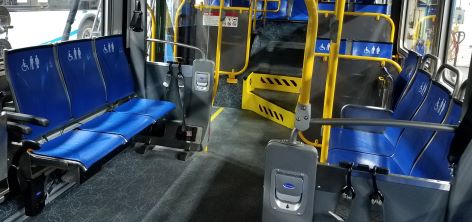 Priority seating on a New Flyer bus: blue seats with decals showing a wheelchair user, pregnant person, and person using a cane