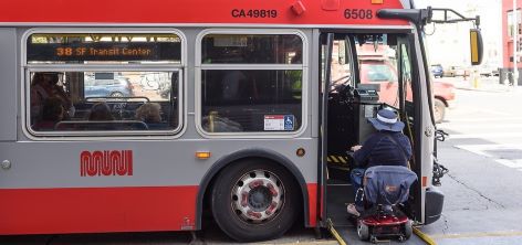 A person using a mobility scooter boards a Muni bus