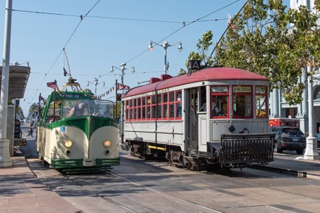 Two vintage streetcars next to each other on the street, one is open air with no roof.