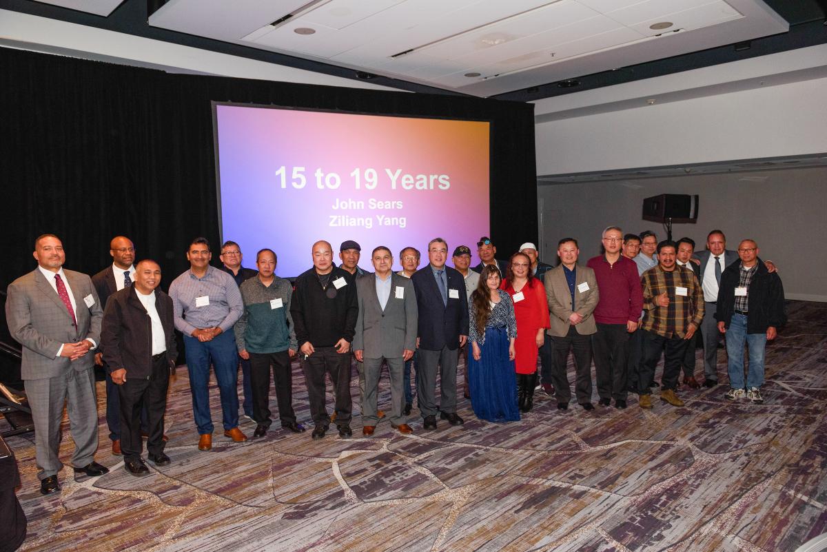 Safe Driver Award winners smile at the 2024 dinner celebrating their work. A crowd poses in front of a projector that says "15 to 19 years" and names two operators.
