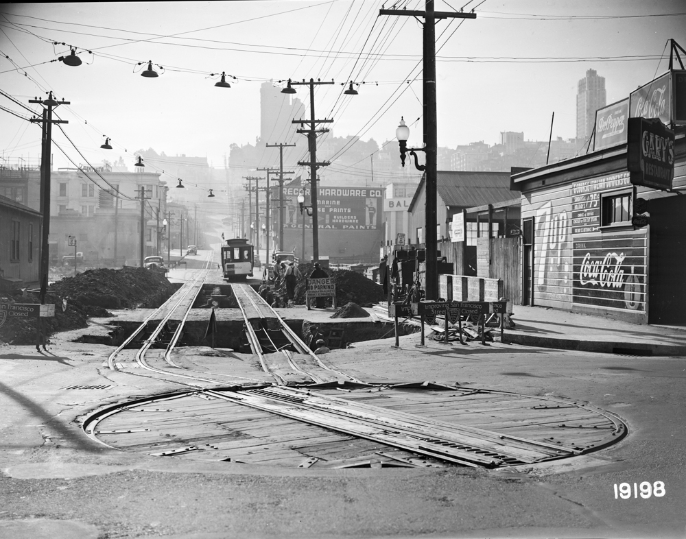 Vintage black and white photo of a cable car traveling past tracks under construction