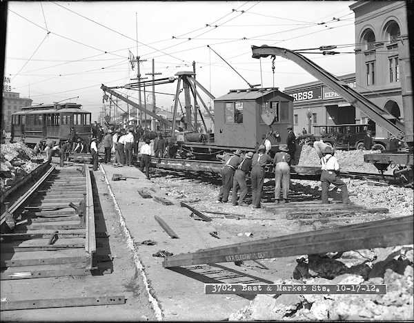 Black and white photo of group of people moving section of tracks with cranes