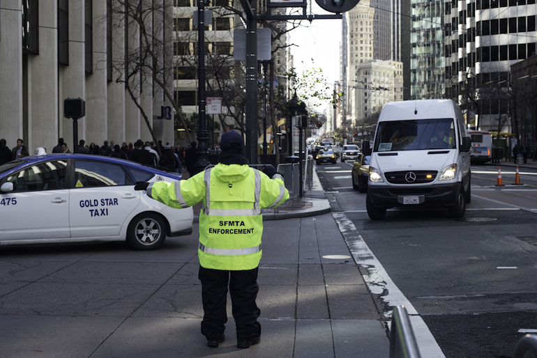 A parking control officer stands on Market Street in yellow cold-weather reflective gear, directing a taxi and delivery truck.
