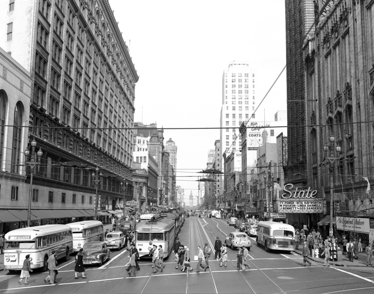 Black and white photograph showing an overhead view of Market Street, looking east from 4th Street.  Pedestrians are walking across Market at the bottom of the frame, with streetcars, buses, and automobiles mid-frame beyond. building facades flank the street at frame left and right.  Photo taken October 1, 1948.