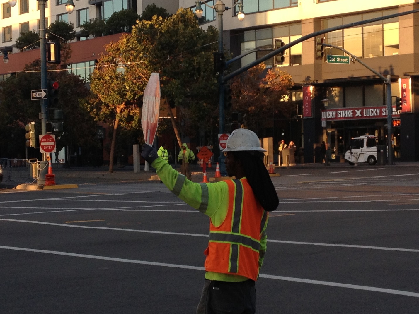 A woman in a safety vest and hard hat holds up a stop sign in the middle of the 4th and King intersection.