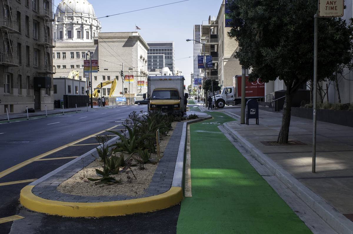 The Polk Street contraflow bike lane with green paint and landscaping, facing north on Polk St. with City Hall in the background