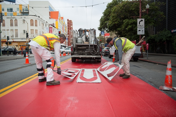 Crew members lay letter stencils to mark a red transit-only lane on Mission Street.