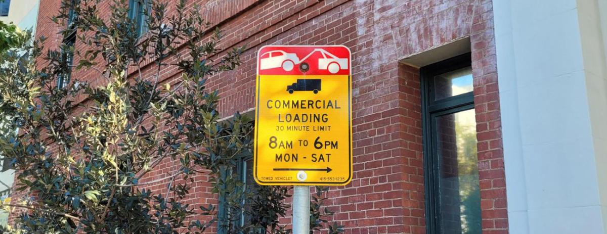 Sign for commercial loading with a red brick building behind it.