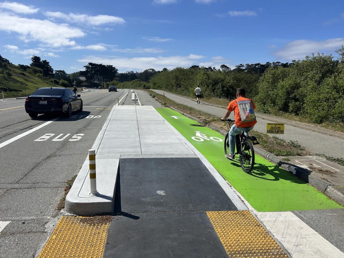 person on bike riding in new bike lane on Lake Merced Blvd next to a new transit boarding island