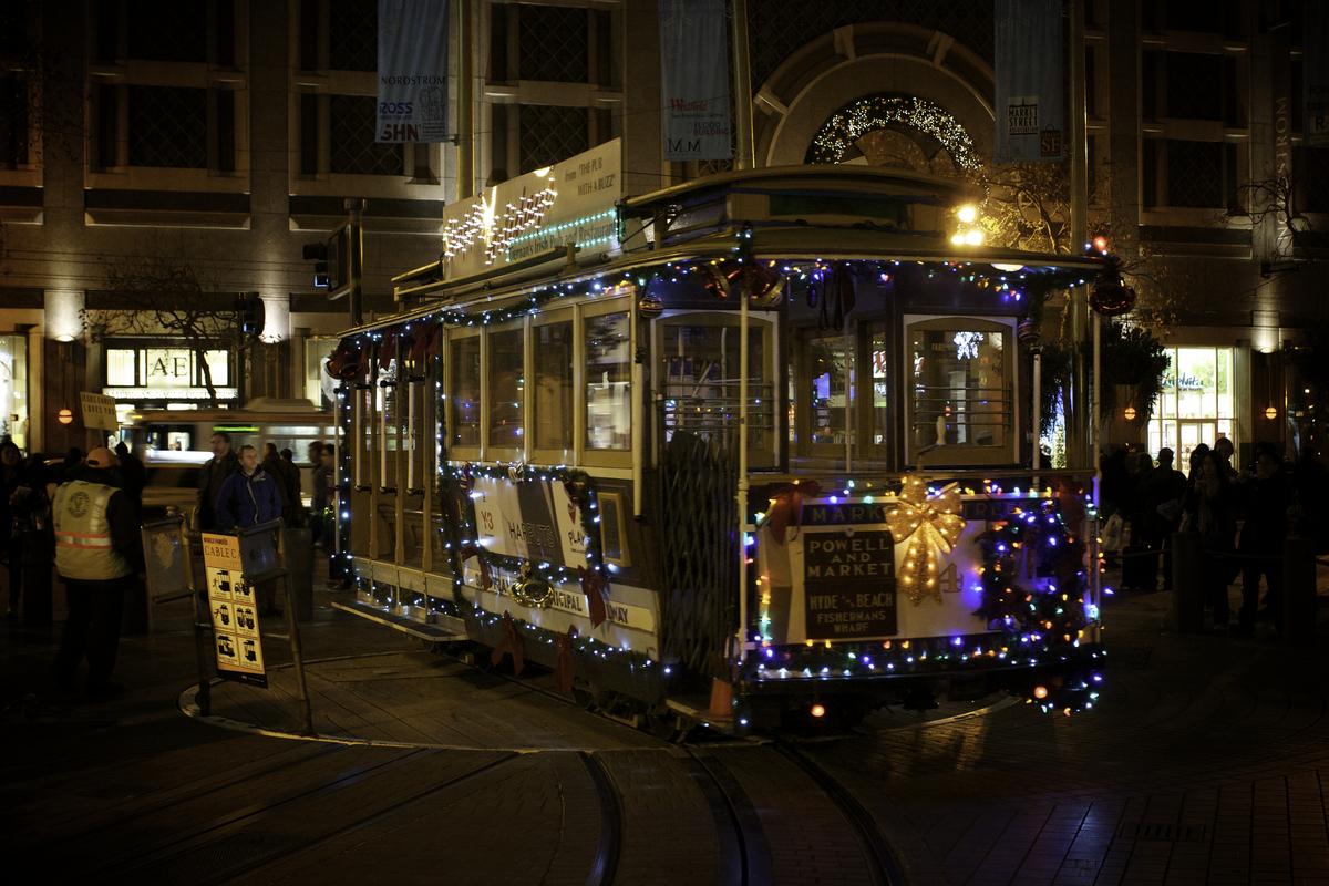 Powell cable car decorated with blue and white twinkle lights on Market Street at night.