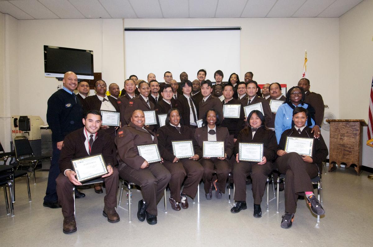 Group of newly graduated Muni transit operators holding certificates at their graduation ceremony.