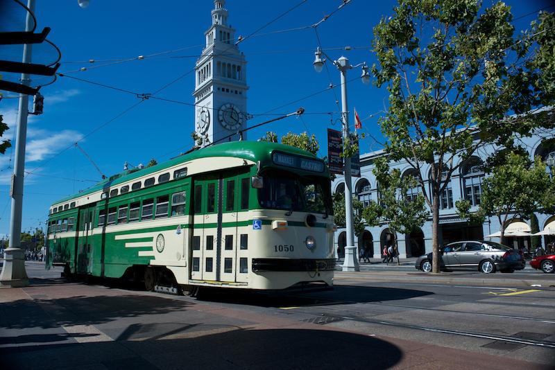 Green and cream historic streetcar numbered 1050 in front of the Ferry Building clock tower on The Embarcadero.