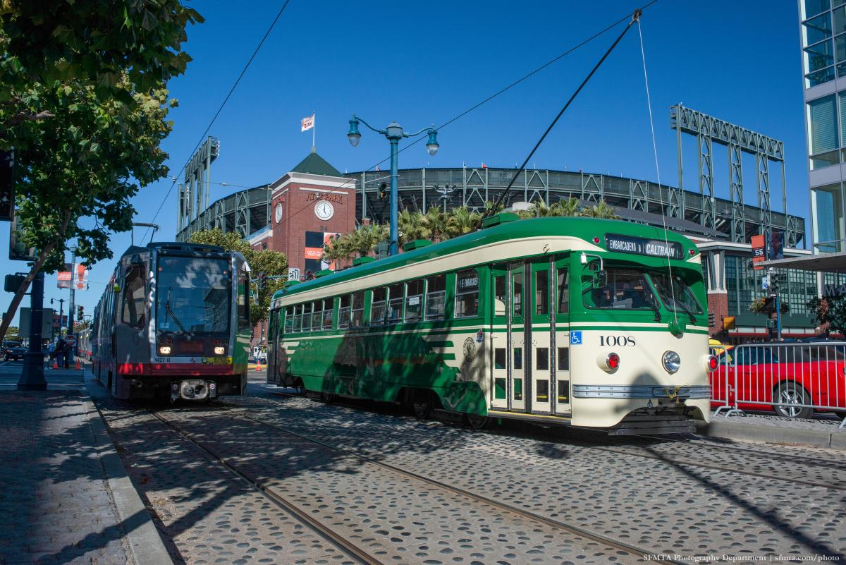 Green and cream vintage streetcar on tracks with baseball stadium in background