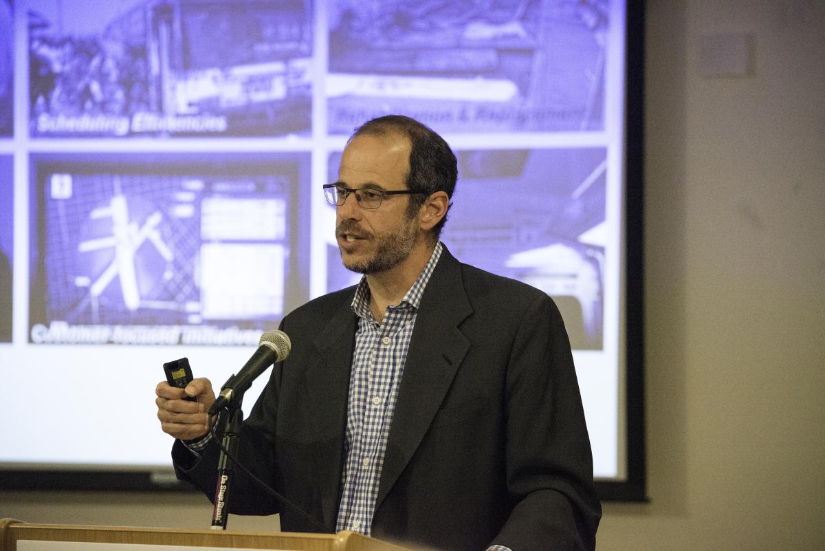 Man in glasses and blazer speaking at podium with microphone during presentation