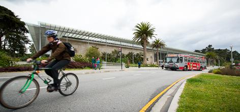 Cyclist riding past California Academy of Sciences building with Muni bus on street