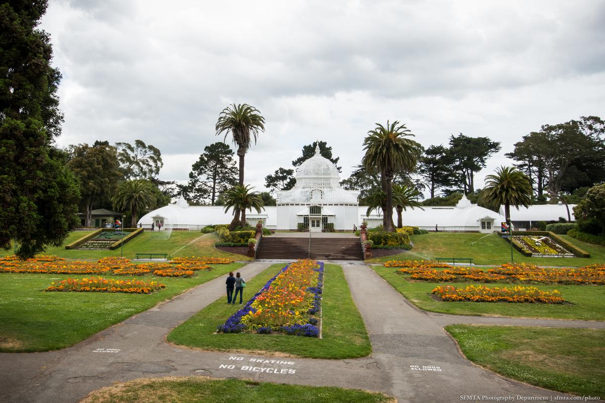 Conservatory of Flowers in Golden Gate Park with colorful flower beds and palm trees lining the pathways.
