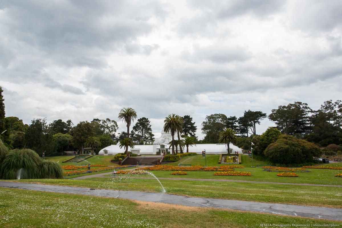 Conservatory of Flowers in Golden Gate Park with manicured gardens and palm trees under cloudy sky