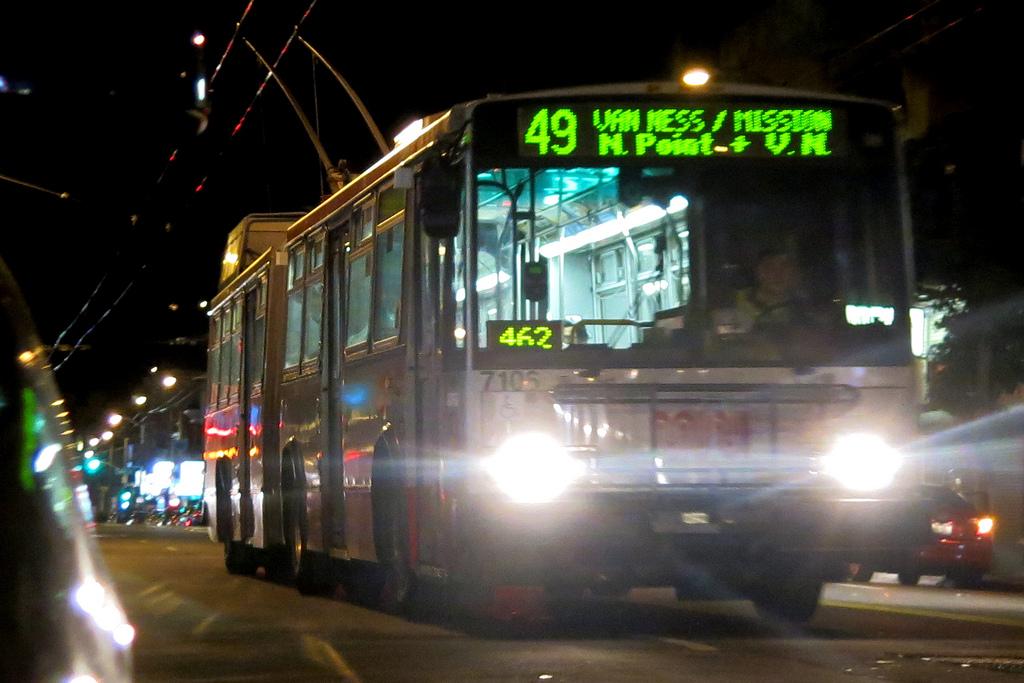 Front of 49 Van Ness/Mission trolley bus on street at night with illuminated headlights and destination display.