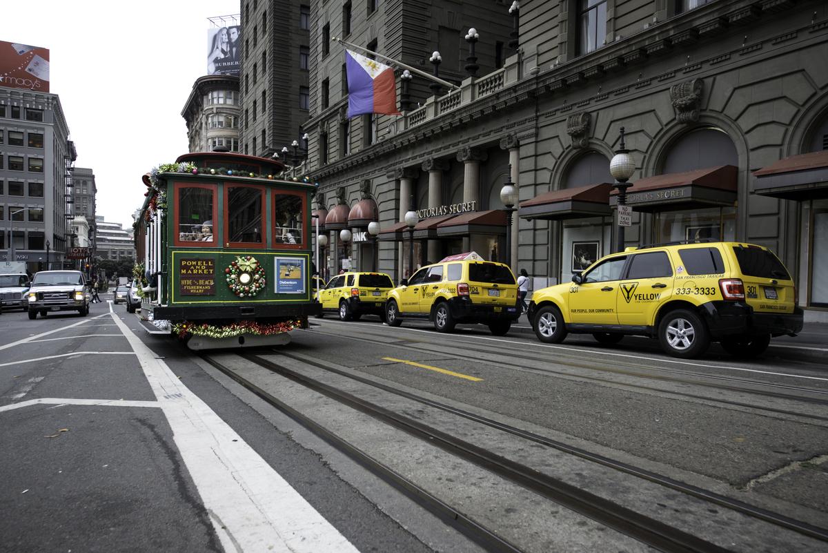 Decorated cable car on Powell Street with yellow taxis and historic building facade behind it.