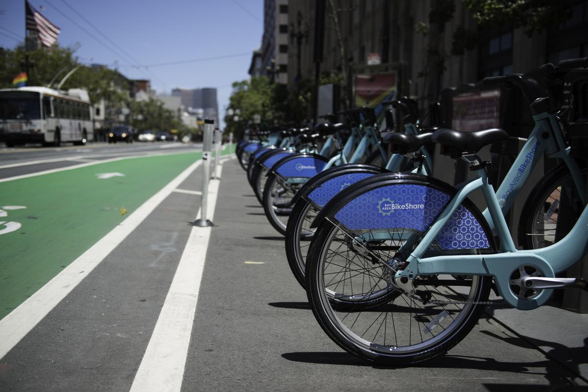 Row of blue bike-share bicycles docked at a station on Market Street with green bike lane visible.