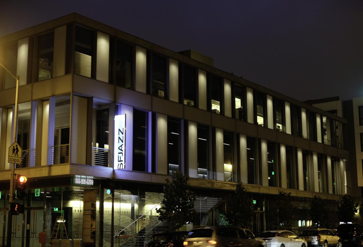 SFJAZZ Center illuminated at night, showing modern multi-story building with vertical columns and blue accent lighting at street level.