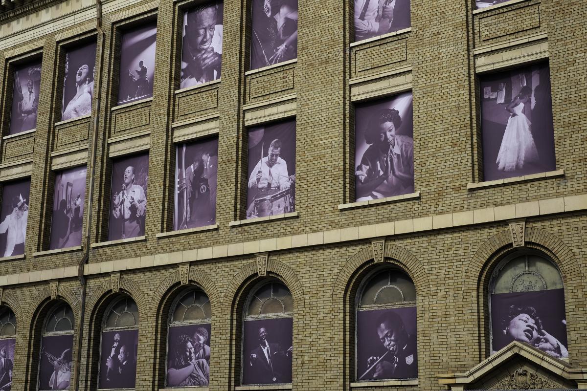 Brick building facade with large windows displaying black and white photographs of jazz musicians and performers.