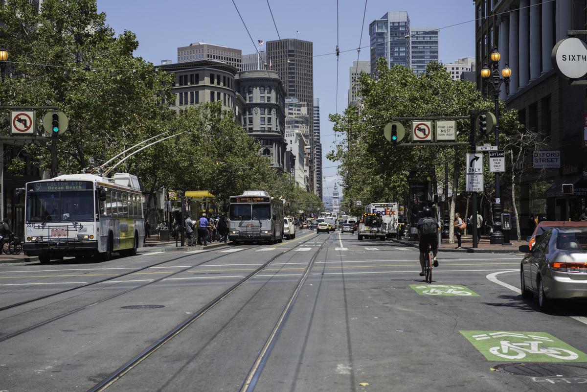 Market Street with cable car tracks, buses, bicyclists, and pedestrians under clear skies.