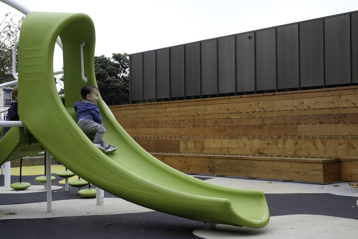 Child sliding down bright green playground slide onto rubber surface