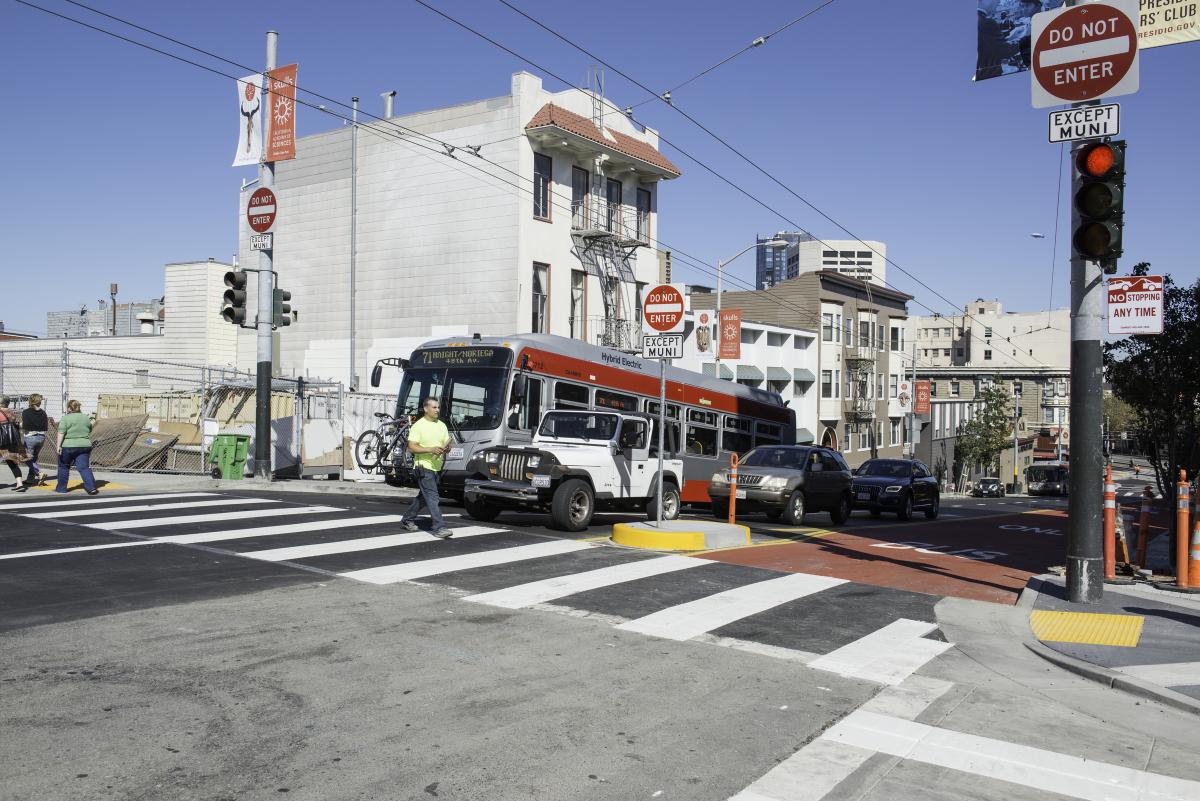 White and orange Muni bus at intersection with pedestrians crossing on Haight Street.
